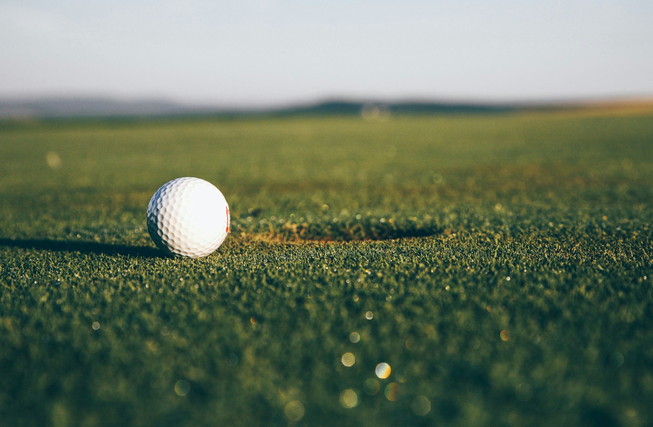 Close up of a golf ball on a green with a hole in the background.